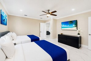 Een hotelkamer met twee bedden, een plafondventilator, een groot schilderij met een strandthema en een donkere dressoir.