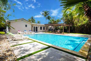 Une piscine avec des chaises longues, un patio couvert et une maison avec un jardin.