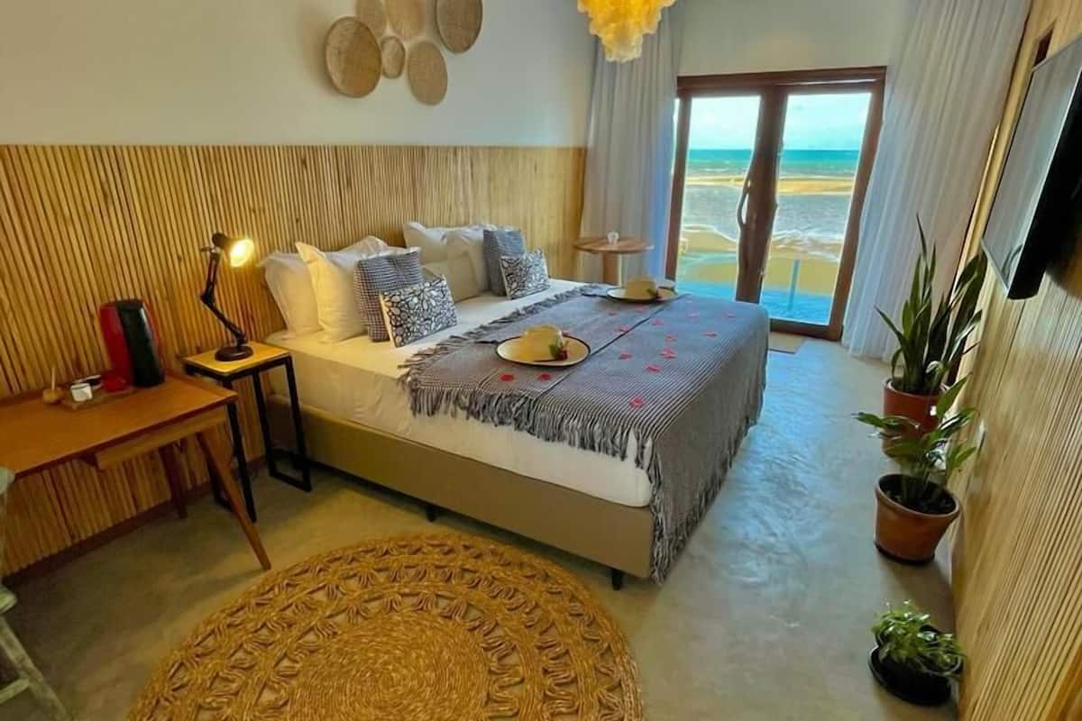 Ein Schlafzimmer mit Bett, Nachttisch, Lampe und Blick auf den Strand.