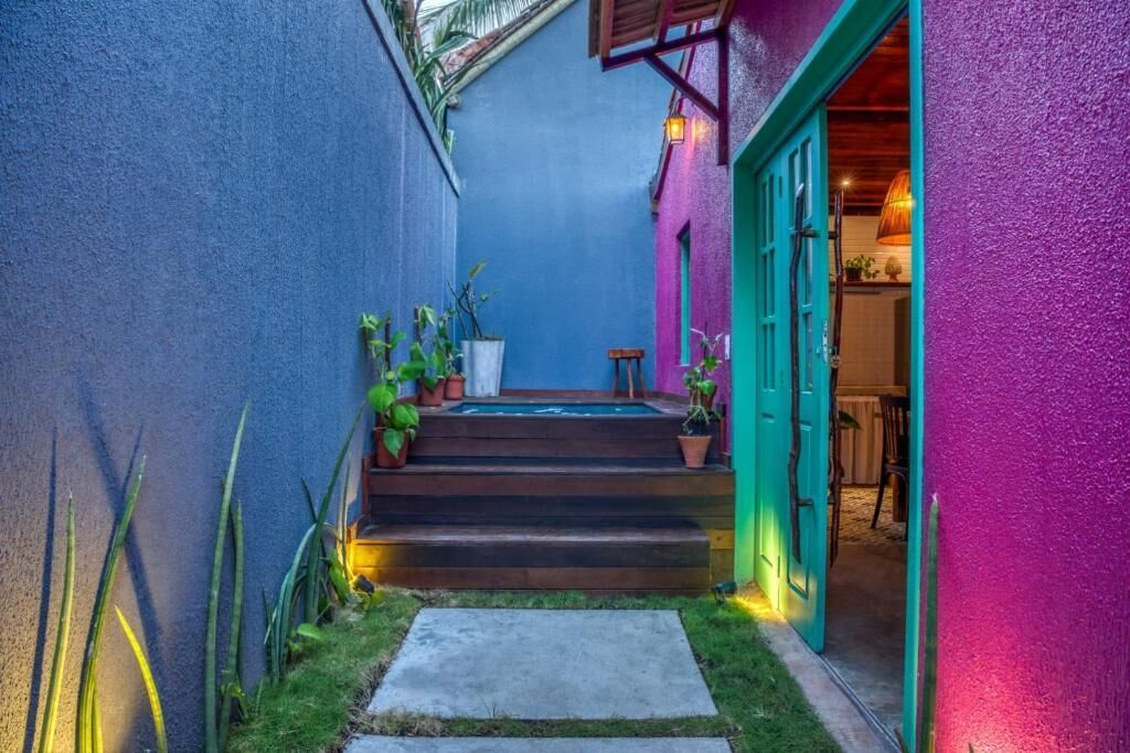 Un estrecho callejón con una escalera de madera que lleva a una puerta, flanqueado por una pared azul y una pared morada.