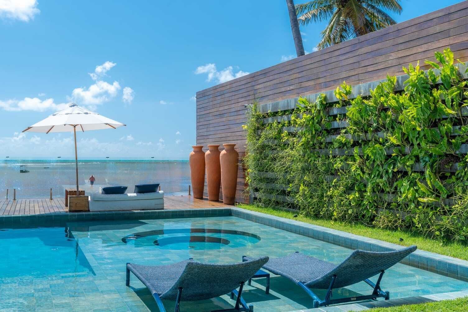 Área da piscina com espreguiçadeiras, deck de madeira e vista para o mar.