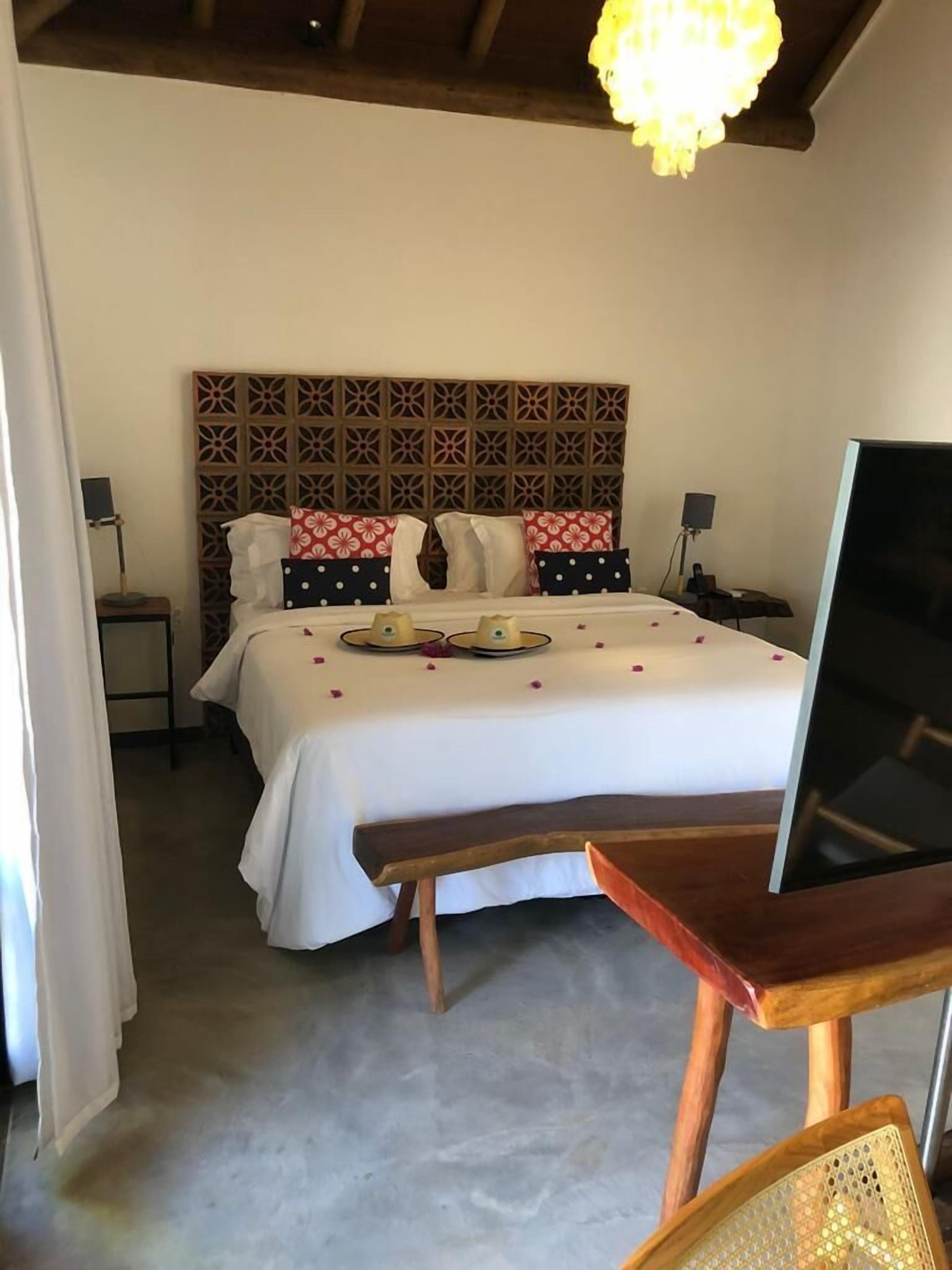 Habitación de hotel con cama, mesita de noche, televisor y un cabecero decorativo.