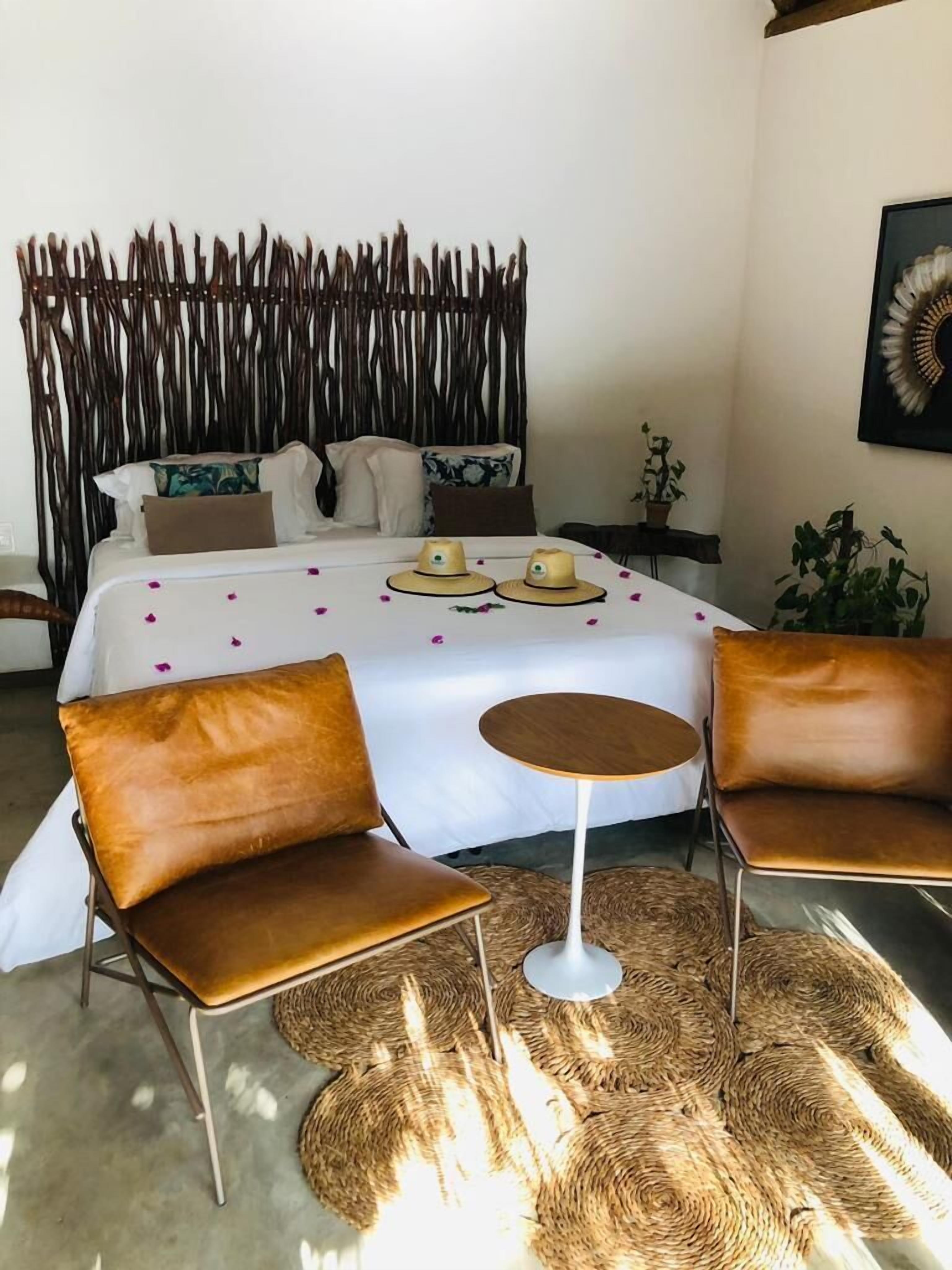 Un dormitorio con una cama, dos sillones de cuero marrón, una mesita redonda y una alfombra tejida.