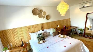 Habitación de hotel con cama, cabecero de madera, zona de comedor con mesa y sillas, y lámpara colgante.