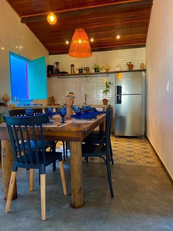 A dining area with a wooden table and chairs, a hanging light fixture, and a kitchen in the background. - Villa Pantai Boutique Hotel Maragogi (Maragogi)