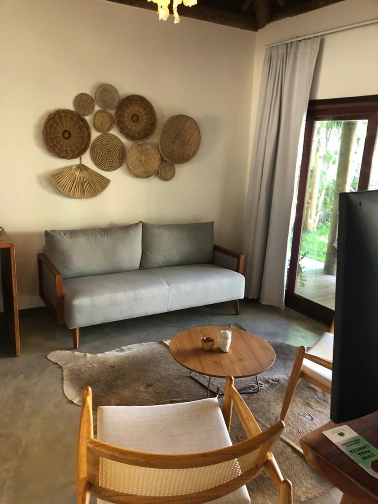 A living room with a grey sofa, a round wooden coffee table, a woven wall hanging, and a view through a glass door.