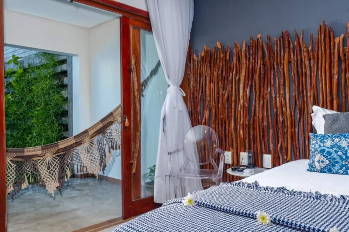 Ein Schlafzimmer mit Bett, Nachttisch, Stuhl, einer Hängematte und Blick ins Grüne.
