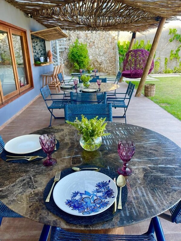 An outdoor dining area with a round table set for four, surrounded by blue chairs. - Villa Pantai Boutique Hotel Maragogi (Maragogi)