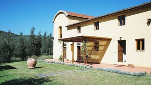 Una casa a due piani con un portico coperto, una grande pianta in vaso e un prato curato.