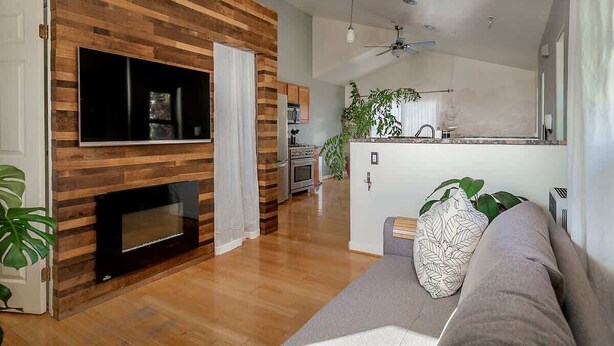 Una sala de estar moderna con pared de madera, televisor de pantalla plana, chimenea y cocina al fondo.