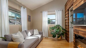 Una sala de estar con sofá, cortinas, una planta grande y chimenea.
