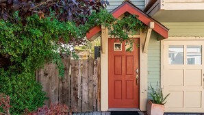 Una casa con puerta roja, cerca de madera y planta en maceta.
