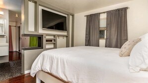 Un dormitorio moderno con una cama grande, un televisor montado en la pared y una ventana con cortinas.
