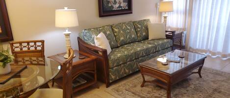 A living room with a sofa, two lamps, a glass coffee table, and a dining table with chairs.