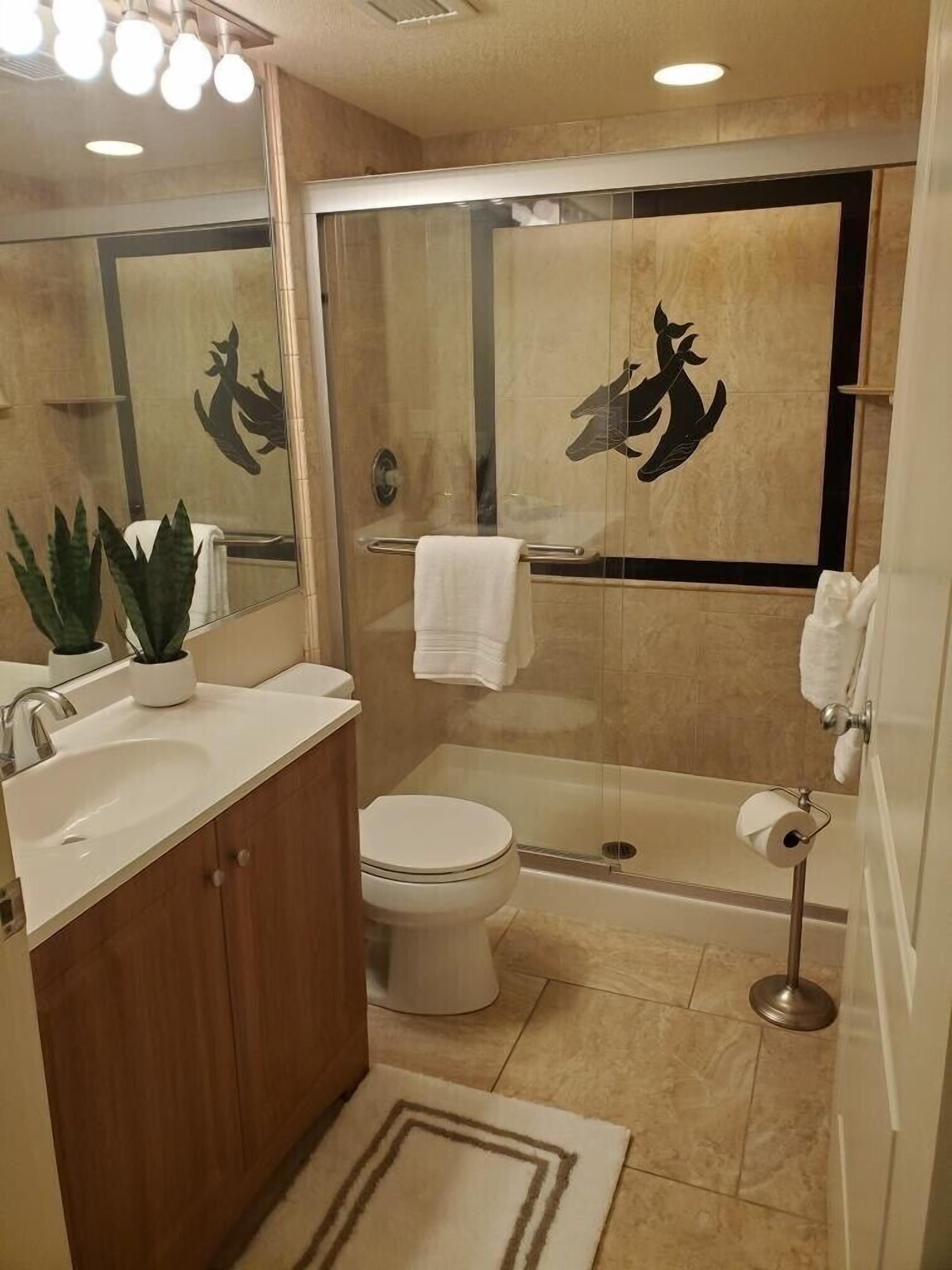 Un bany modern amb dutxa de vidre, vàter i un lavabo amb mirall a sobre.