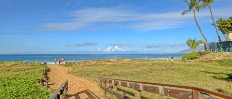 A wooden boardwalk leading to a beach with a clear view of the ocean and palm trees.