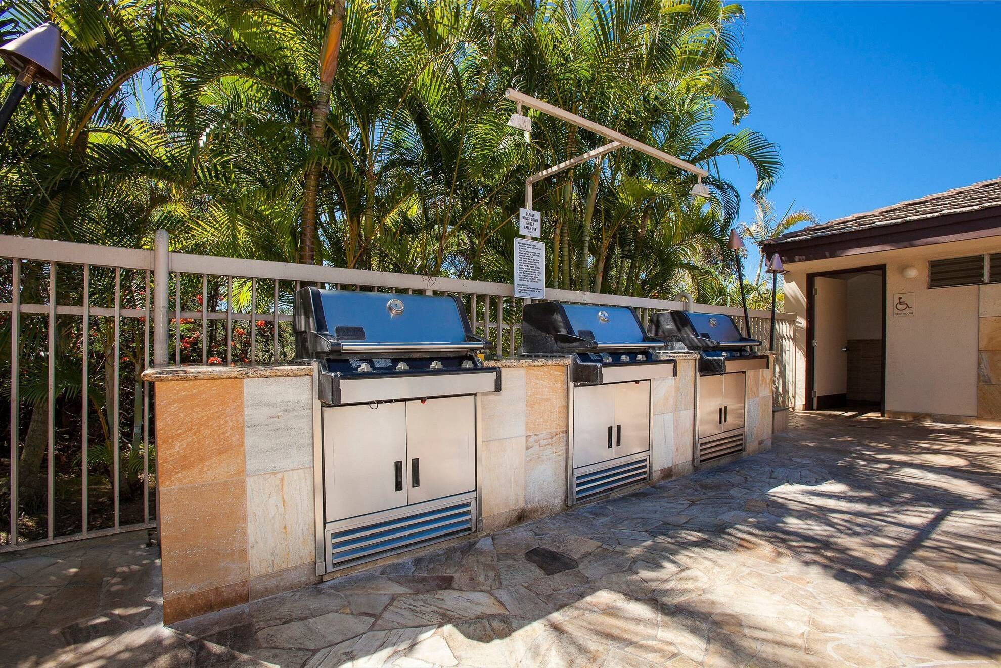 Una hilera de parrillas para barbacoa con un cartel arriba, una entrada accesible para sillas de ruedas y una zona de patio con suelo de piedra.