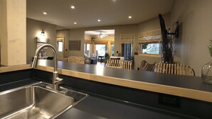 Une cuisine moderne dotée d’un évier en acier inoxydable, d’un coin repas avec des chaises en osier et d’un ventilateur de plafond.