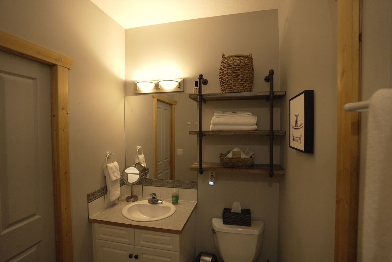 A bathroom with a sink, mirror, towel rack, toilet, and shelves with towels and a basket.