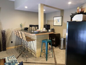 A compact kitchen with a central island, bar stools, a refrigerator, and a microwave.