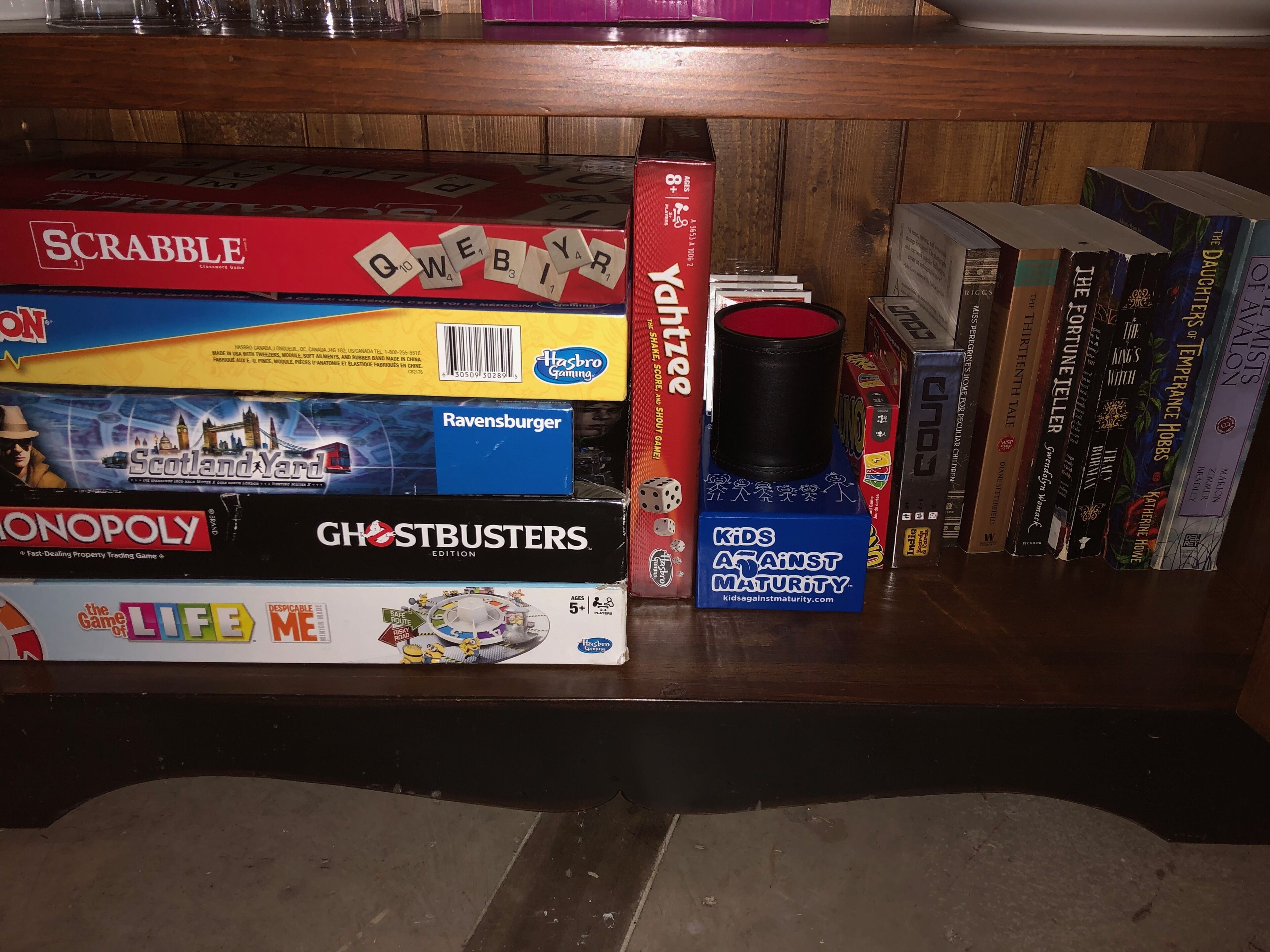 A shelf with various board games and books, including Scrabble, Ghostbusters, and The Game of Life.