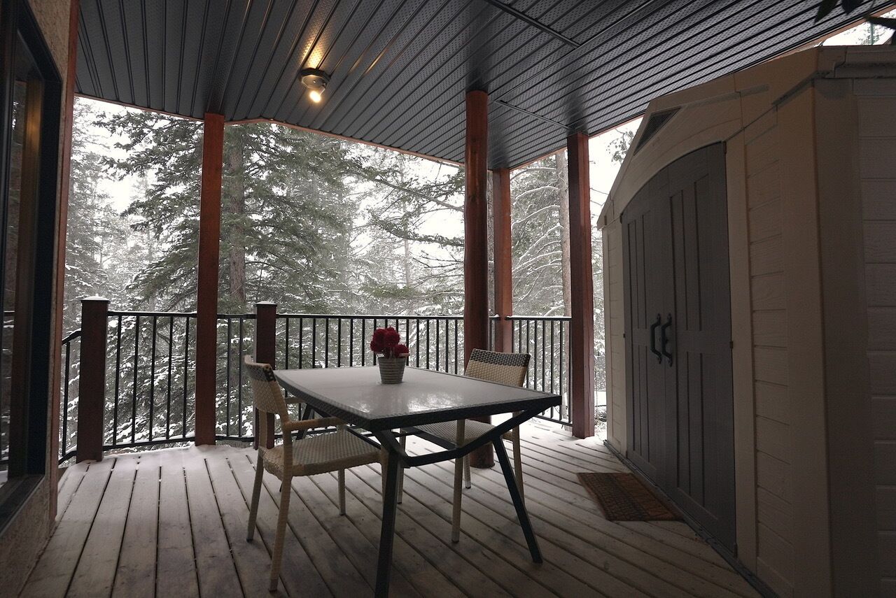 Een houten terras met een tafel en stoelen, uitkijkend op een besneeuwd bos.