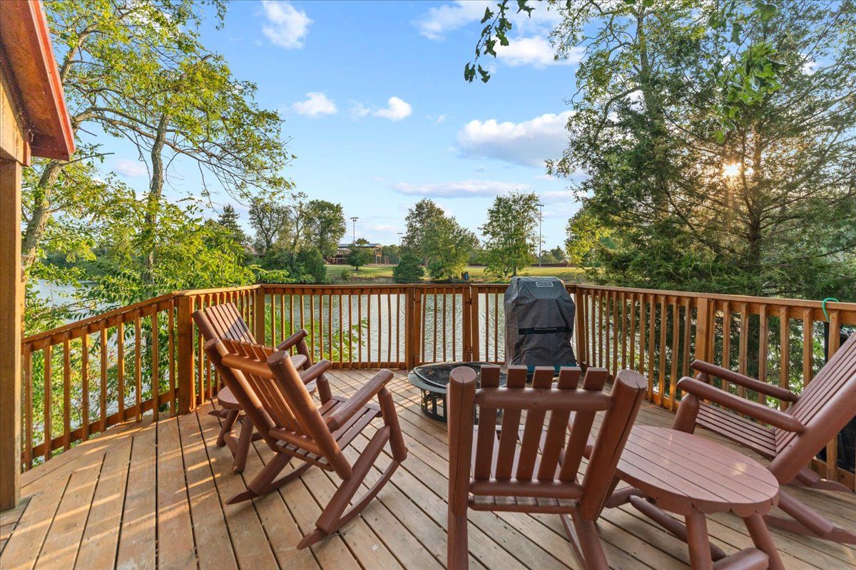 Une terrasse en bois avec des fauteuils à bascule et un barbecue, offrant une vue sur une étendue d’eau et des arbres.