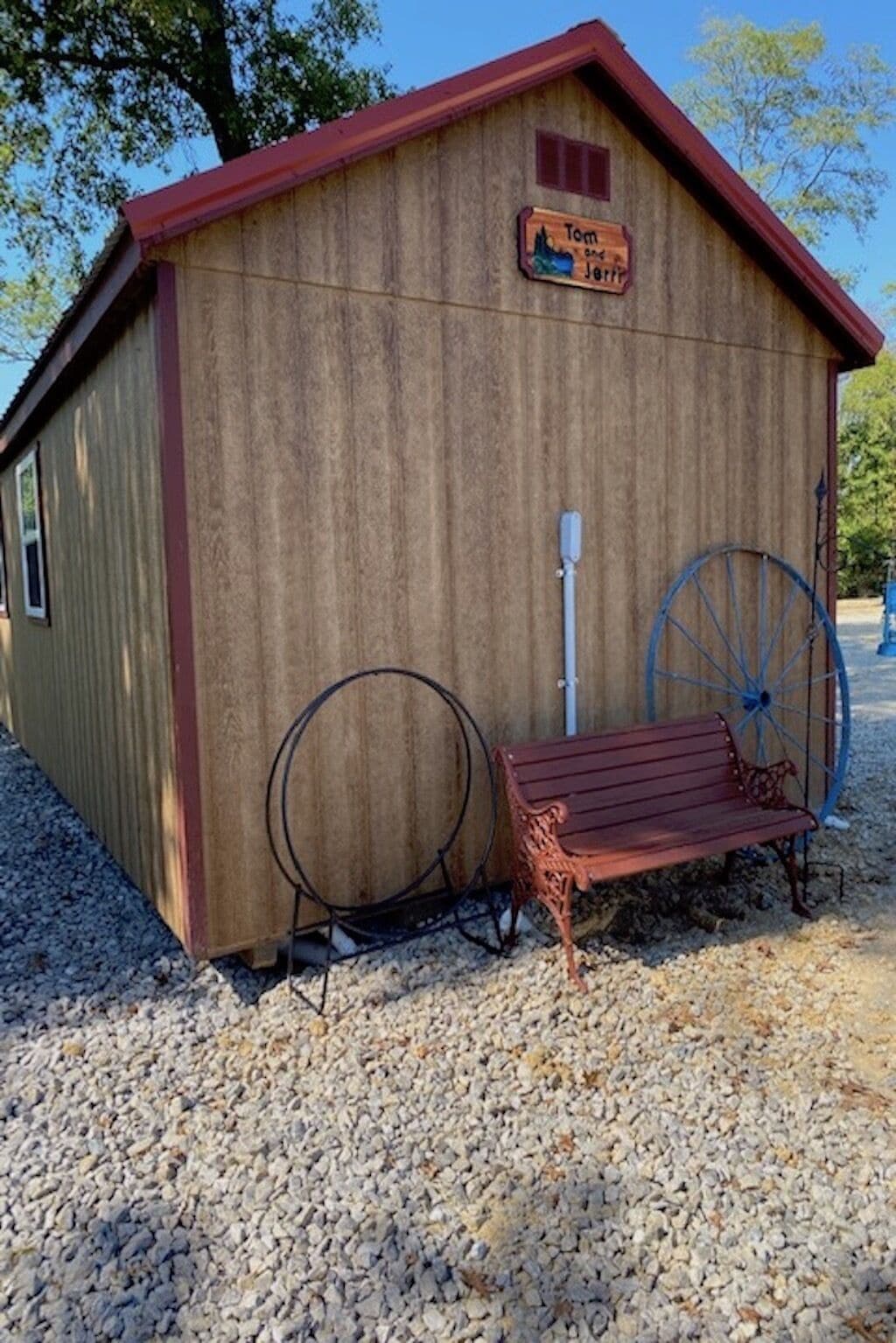 A wooden shed with a red roof, a bench, and a large blue wheel.