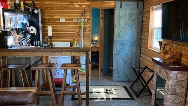 Een rustiek houten interieur met een bar, krukken, een bank en een stenen openhaard.