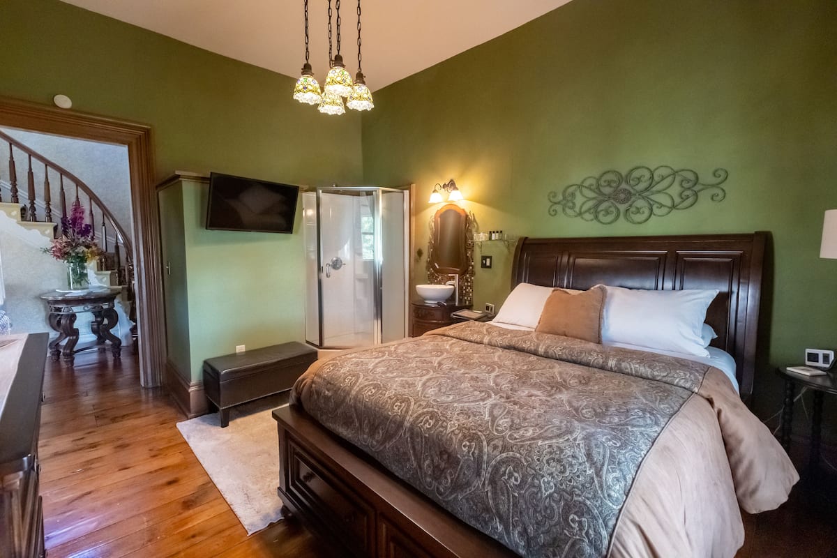 A bedroom with a large bed, a dresser, a vanity, and a staircase leading to another level.