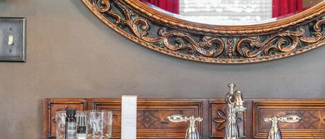 A wooden vanity with a large ornate mirror, a white sink, and toiletries.