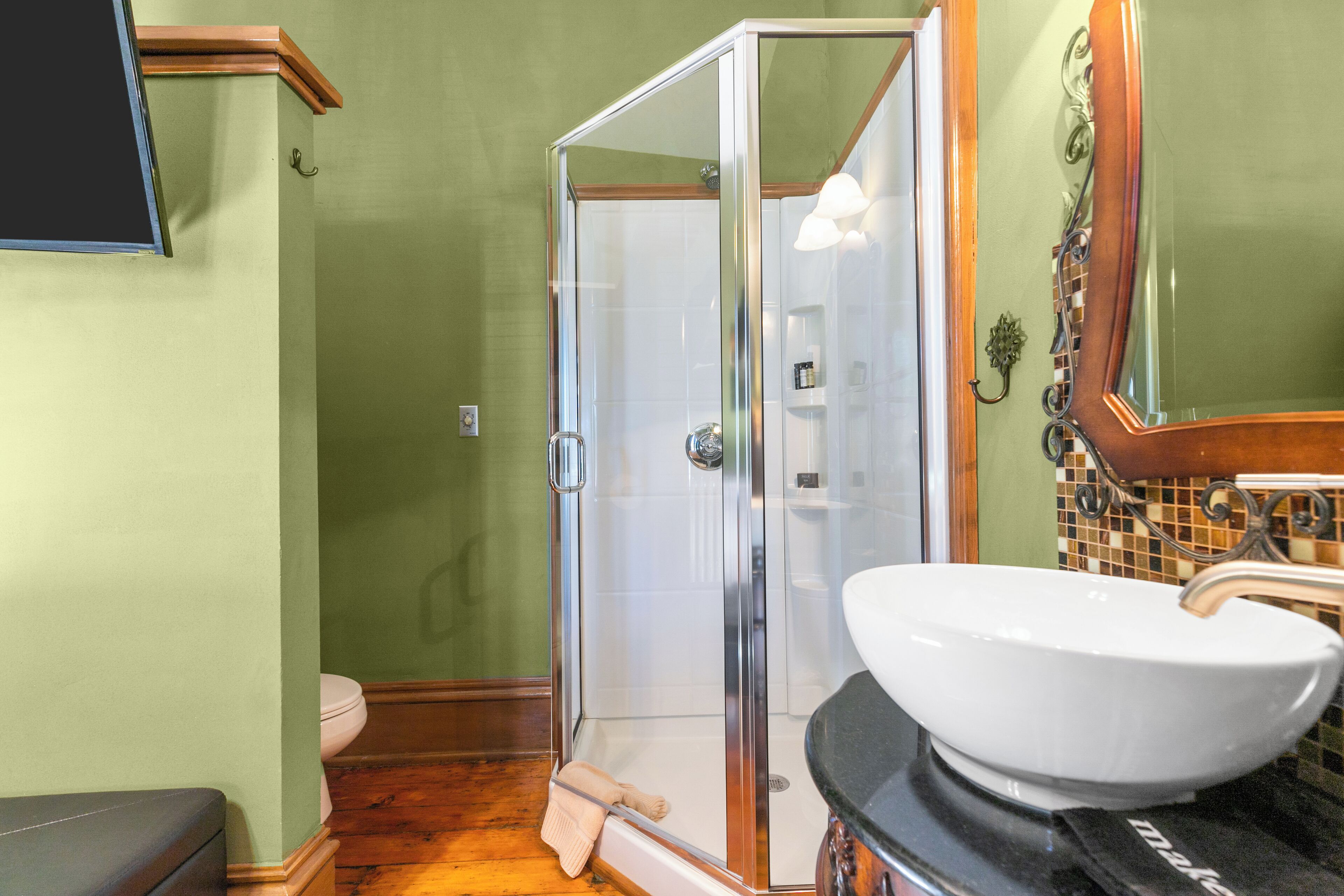 Une salle de bain avec une douche à parois de verre, un lavabo blanc et un plancher en bois.