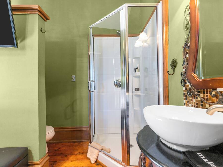 Une salle de bain avec une douche à parois de verre, un lavabo blanc et un plancher en bois.