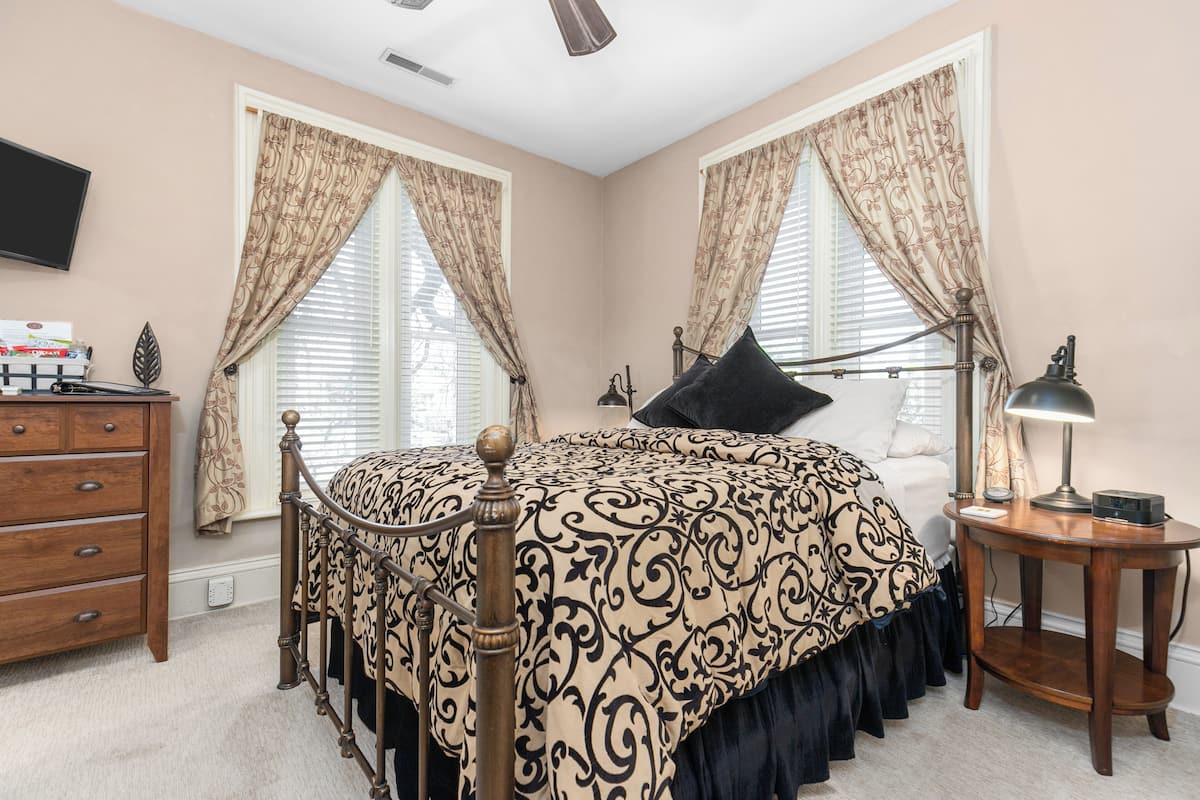 A bedroom with a bed, dresser, bedside table, lamp, and curtains.
