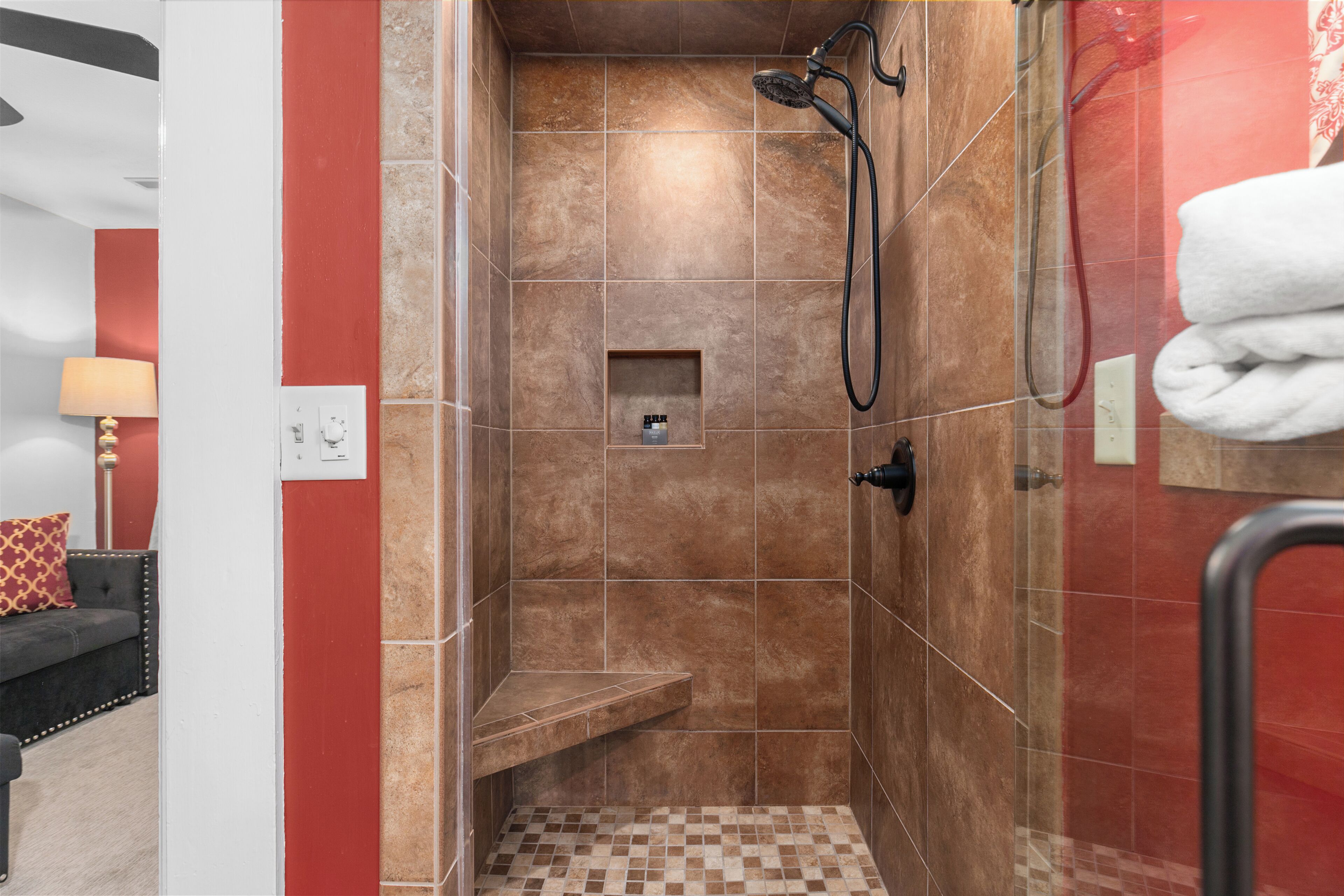A shower area with brown tiles, a shelf, and a towel rack.