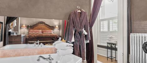 A hotel room with a large mirror, a white bathtub, a wooden bed, and a window with curtains.