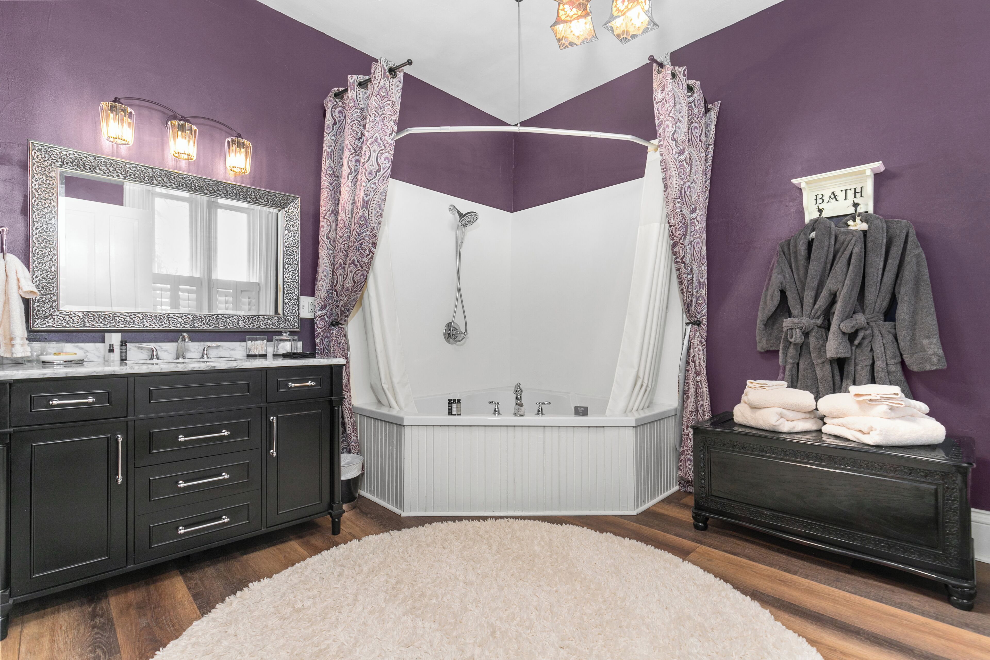 Une salle de bain avec une baignoire sur pieds, un meuble-lavabo avec des placards sombres et un tapis blanc moelleux.