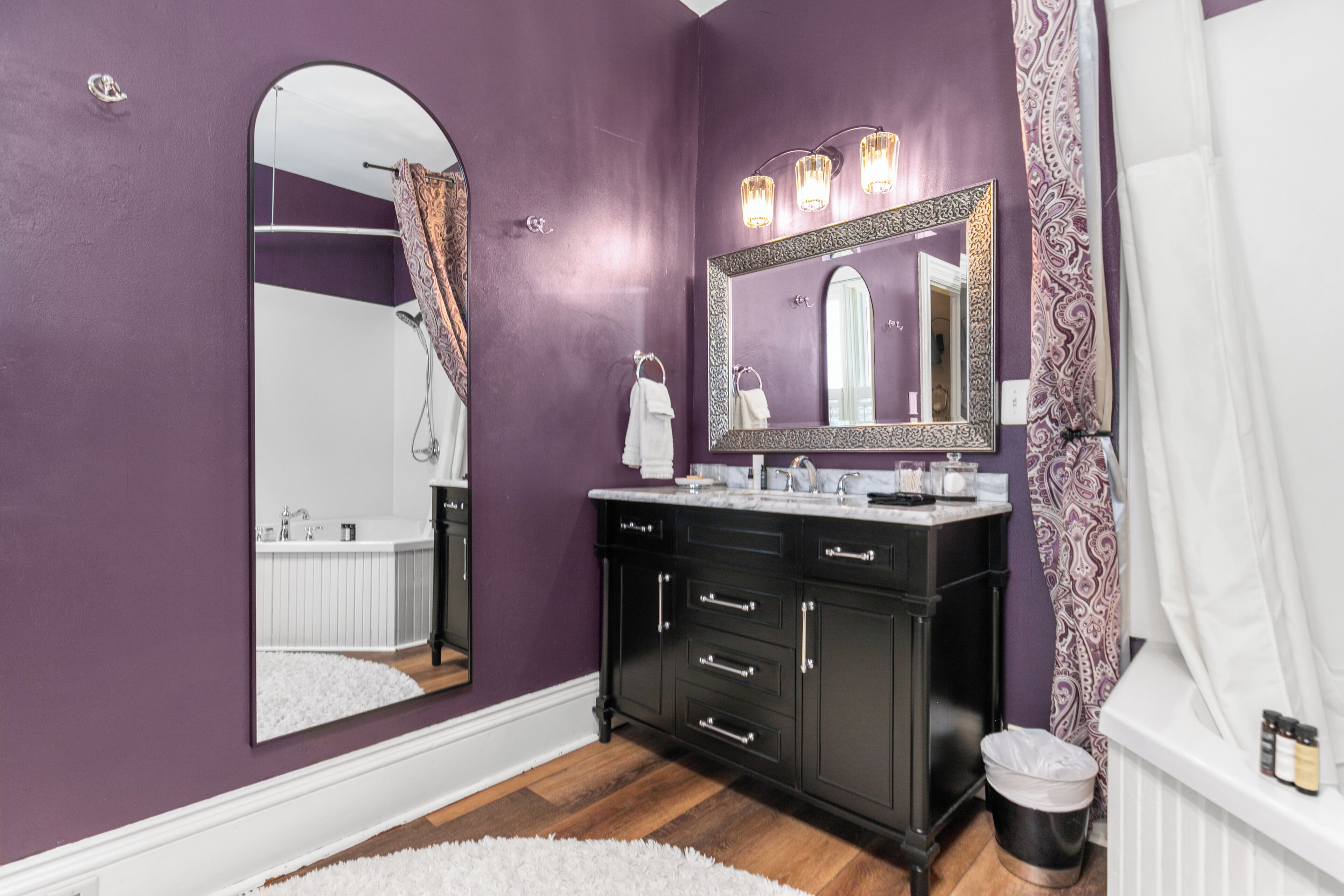 Un baño con paredes moradas, un espejo grande, un tocador negro y un lavabo blanco.