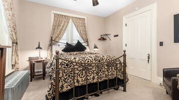 A bedroom with a bed, a ceiling fan, a window with curtains, a door, and a coat rack.