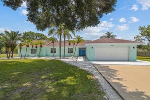 A single-story house with a light green exterior, a blue door, and a white garage door. - Private Lakefront Retreat with Heated Pool, Dock & Kayaks Near Tampa (Tampa)