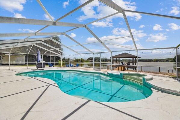 A covered swimming pool with a clear blue water feature, surrounded by a white deck and a pergola structure. - Private Lakefront Retreat with Heated Pool, Dock & Kayaks Near Tampa (Tampa)