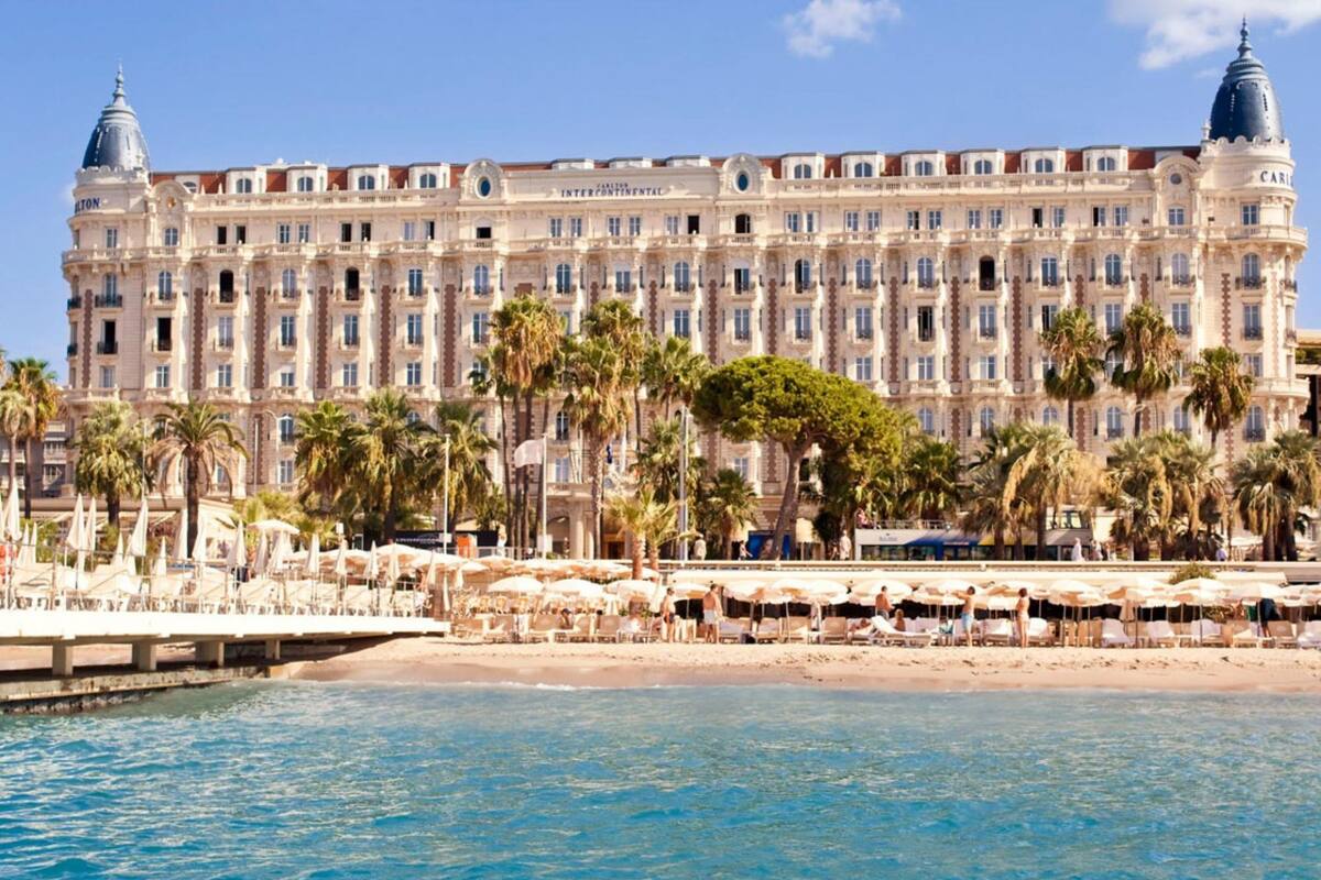Ein großes, historisches Hotel mit einer prachtvollen Fassade, Palmen und einem Strand im Vordergrund.