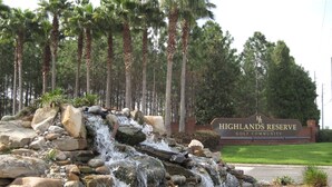 Schild für die Highlands Reserve Golf Community mit einem Wasserfall und Palmen im Hintergrund.
