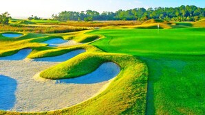 Campo de golf con búnkeres de arena, un putting green y un mástil de bandera.