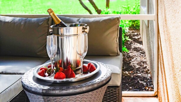 A wicker chair with a cushioned seat and a metal tray holding a champagne bottle and glasses, with strawberries on the tray. - 2 Room PGA Village Golf Villa Suite by Clubhouse (Port Saint Lucie)