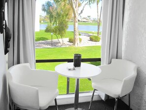 A room with two white chairs and a small table with a black object, overlooking a well-maintained lawn and a body of water. - 12 Room Scottsdale Golf Tennis Lake Resort Villa (Paradise Valley)