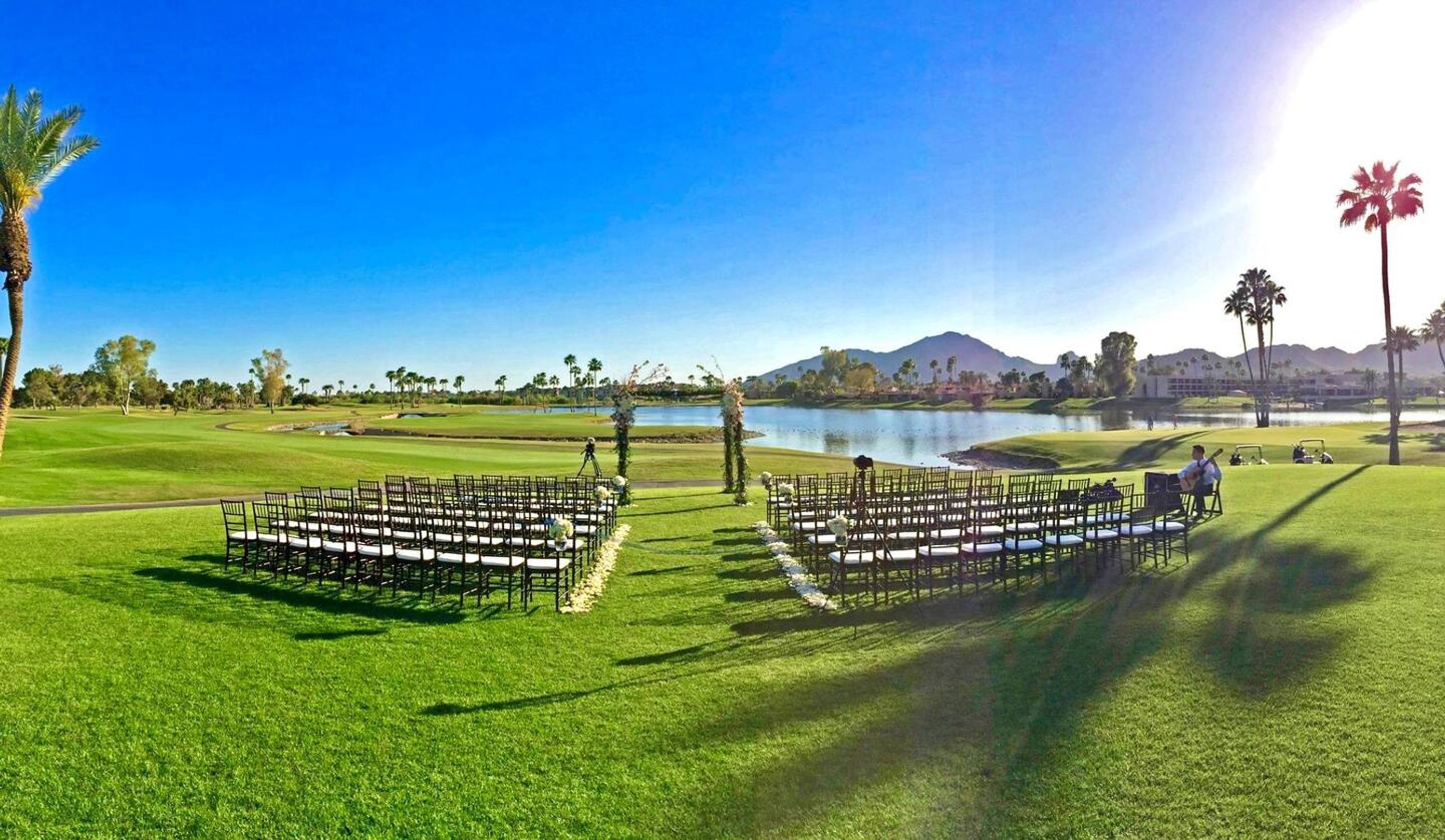 A golf course with a lake, palm trees, and a clear sky.