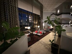 Un moderno vestíbulo de hotel con área de descanso, ventanas amplias y plantas decorativas.