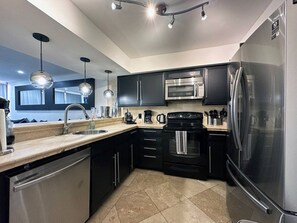 A modern kitchen with stainless steel appliances, black cabinets, and pendant lighting.