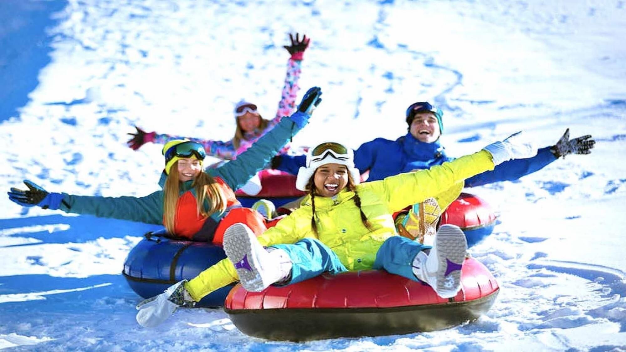 Personas deslizándose en neumáticos sobre nieve en una pendiente nevada.
